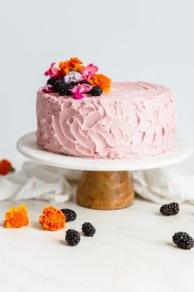 Best Chocolate Cake with Blackberry Buttercream displayed on a cake plate and topped with blackberries and flowers