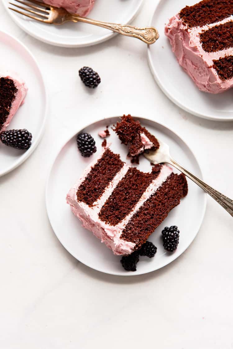 Overhead shot of Chocolate Three Layer Cake with Blackberry Buttercream slices on white plates with forks and garnished with fresh blackberries