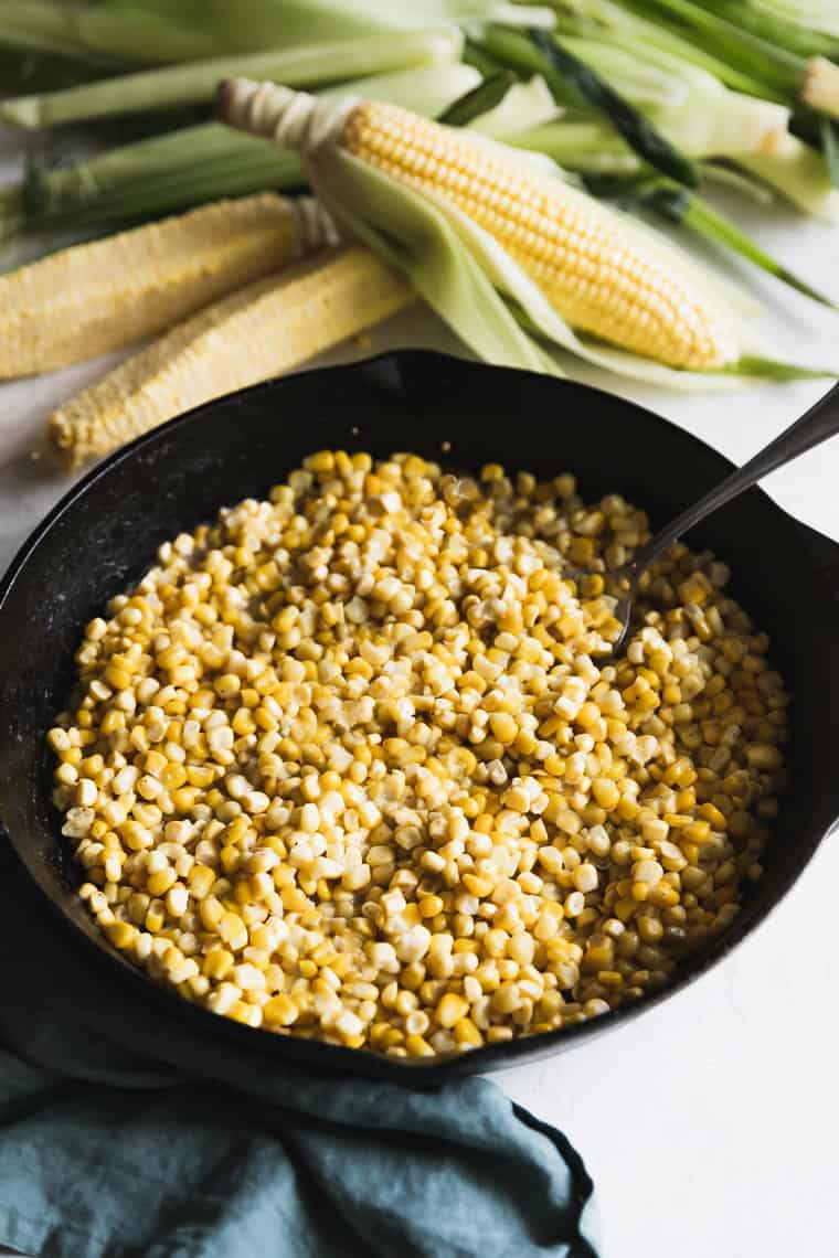Fried corn in a black cast iron skillet with shucked corn on the cob in the background