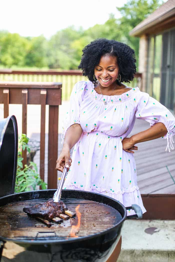 Jocelyn holding with tongs over a BBQ grill next to a flame on the right coming up from burning charcoal