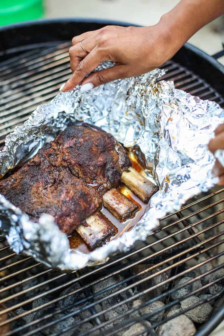 Beef ribs wrapped in aluminum foil over a BBQ grill