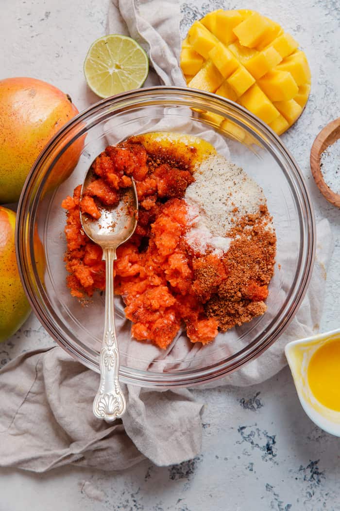 Mango Jerk Salmon Burger ingredients all in a glass bowl ready to be mixed together next to fresh mangoes and lime