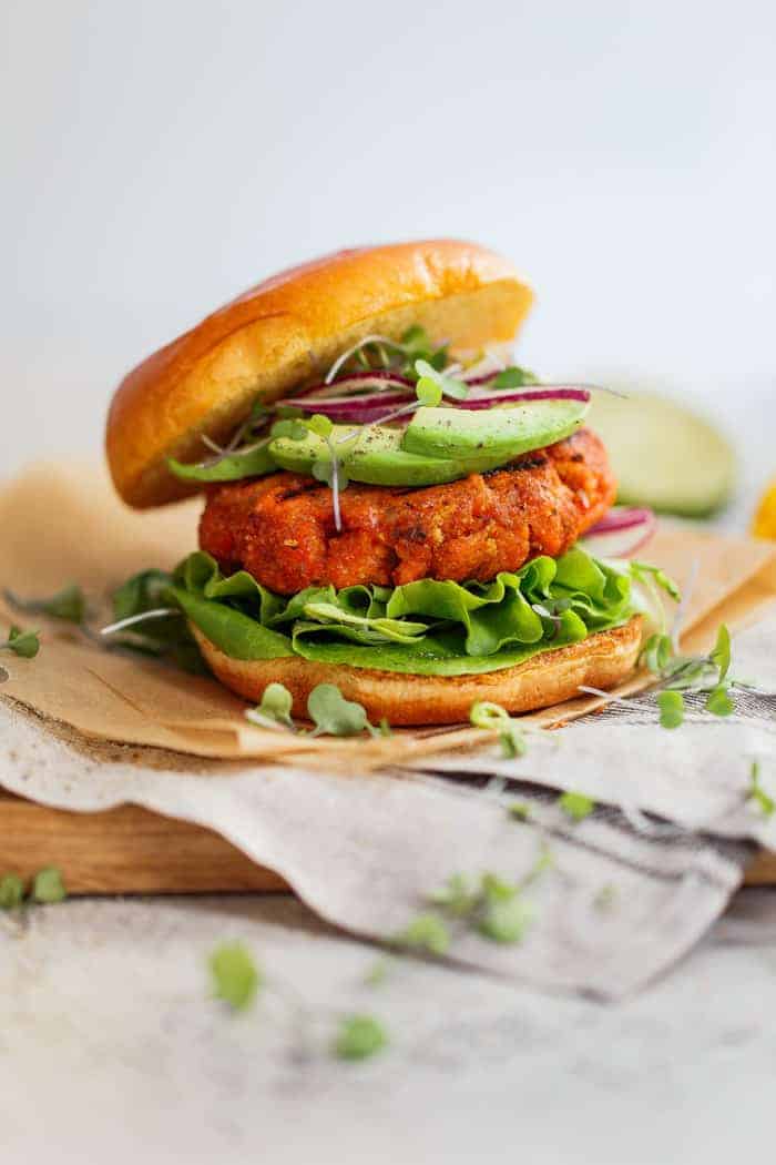 Close up of a completed mango jerk salmon burger with all the fixings served on top of parchment paper and a wooden cutting board