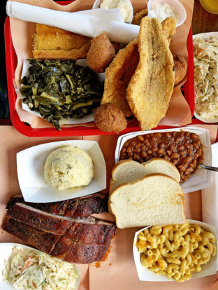 Overhead shot of soul food classics at Rodney Scott's including greens, fried fish, hush puppies, ribs, baked beans and mac and cheese