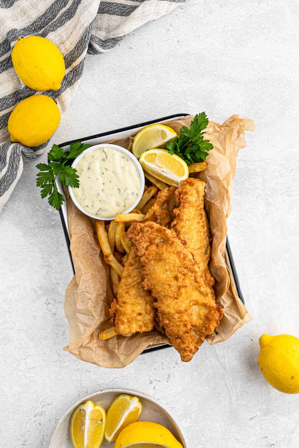 A tray of fish and chips on the table with lemons and tartar sauce.