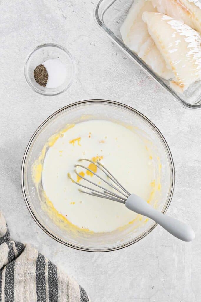 Milk added to the batter and a whisk in the bowl to stir.