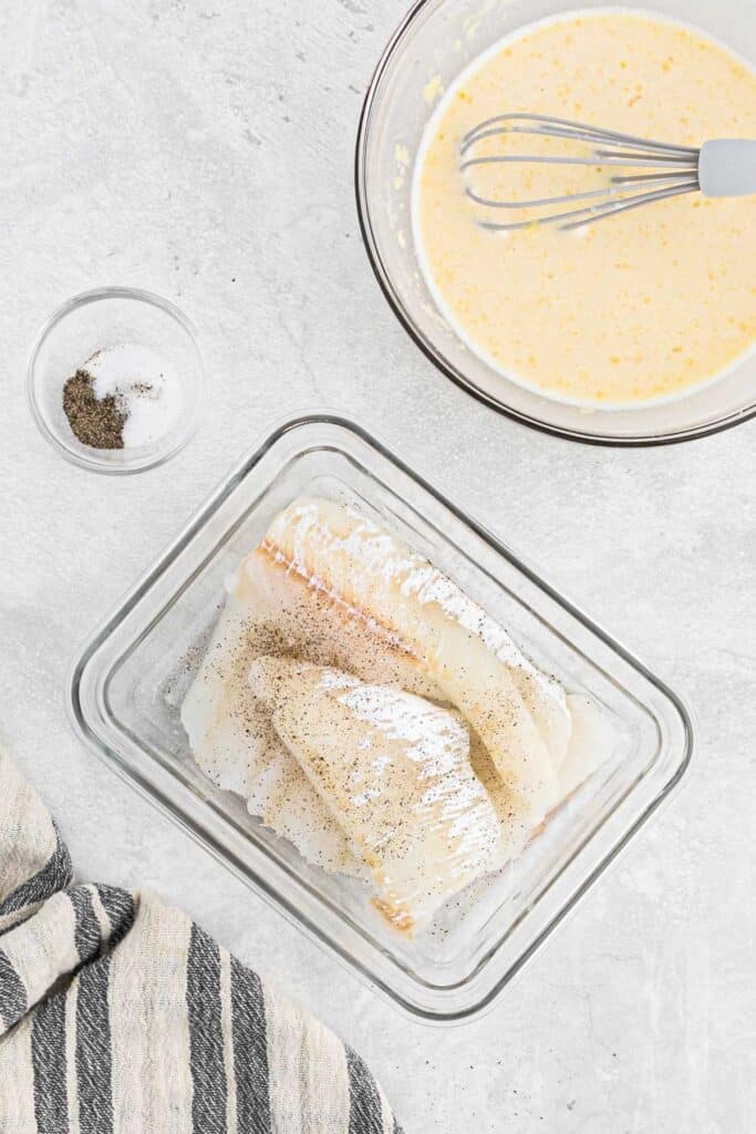Fish in a container of flour and batter in a bowl next to it.