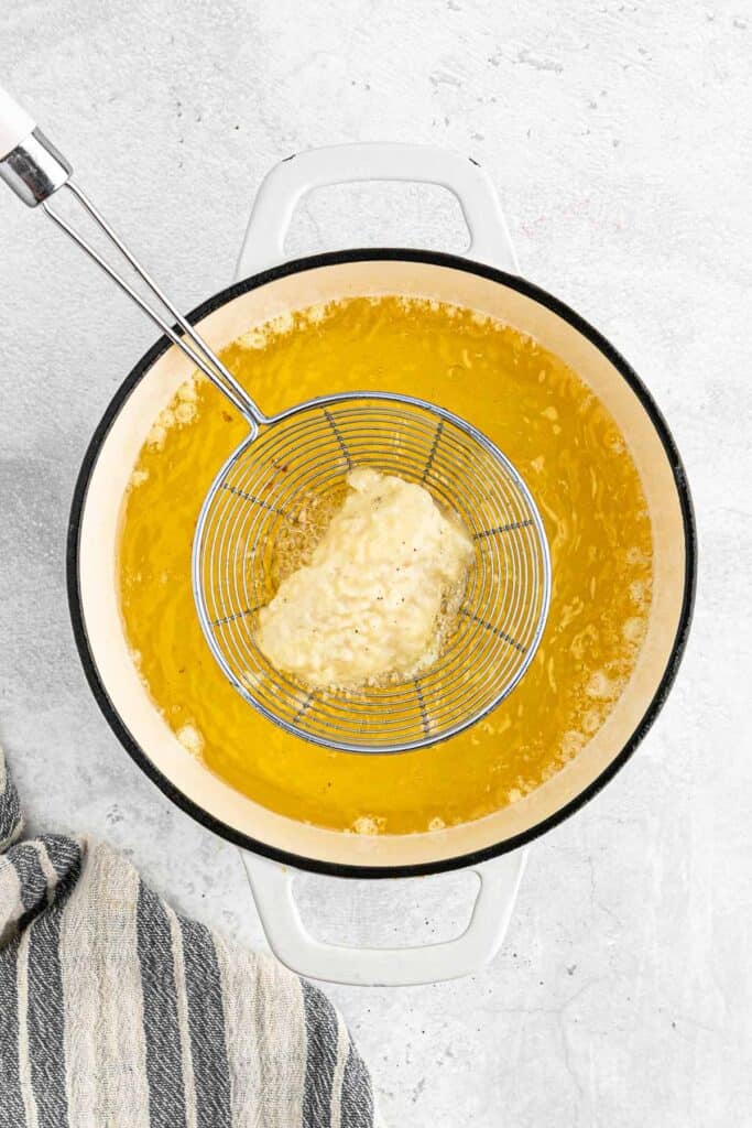 A piece of fish in a strainer over the hot oil.