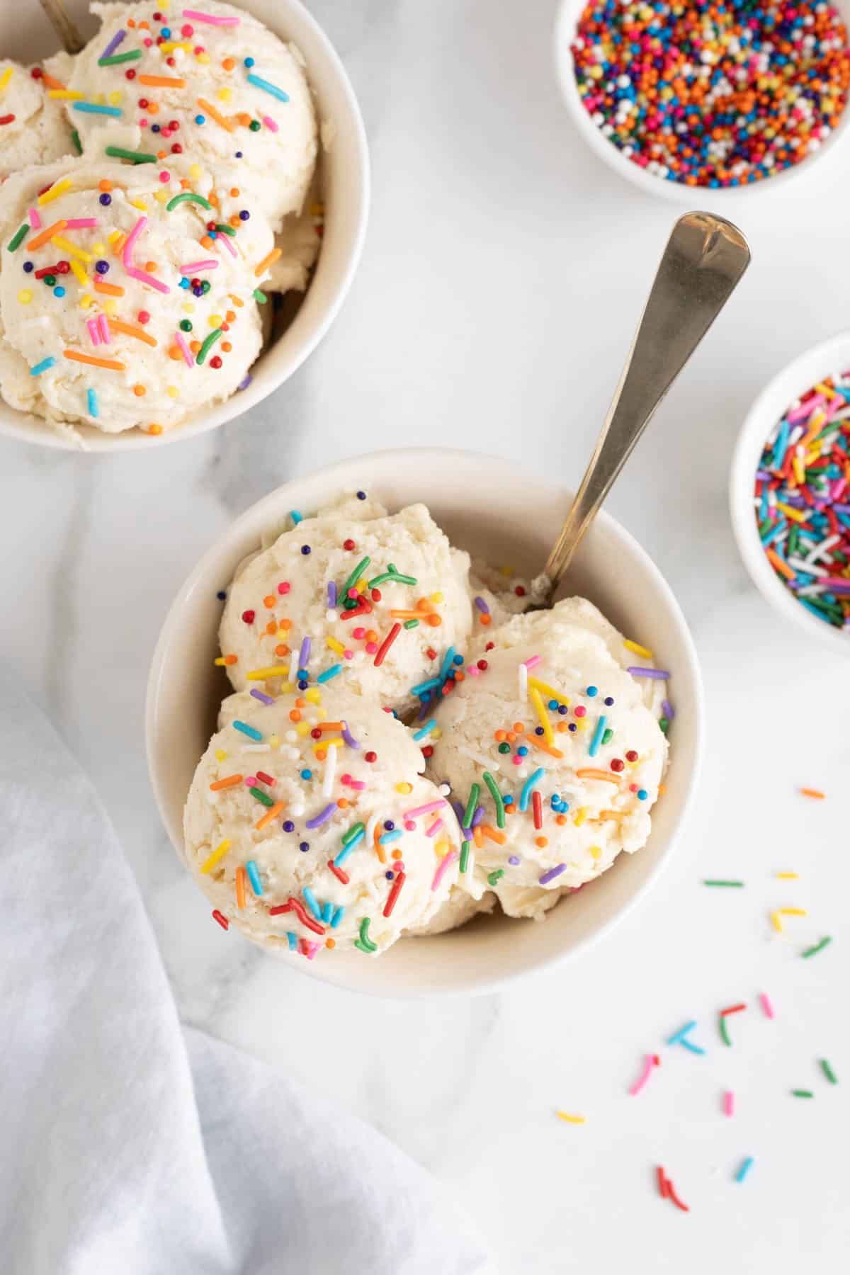 Overhead shot of two bowls filled with scoops of homemade vanilla ice cream topped with rainbow sprinkles