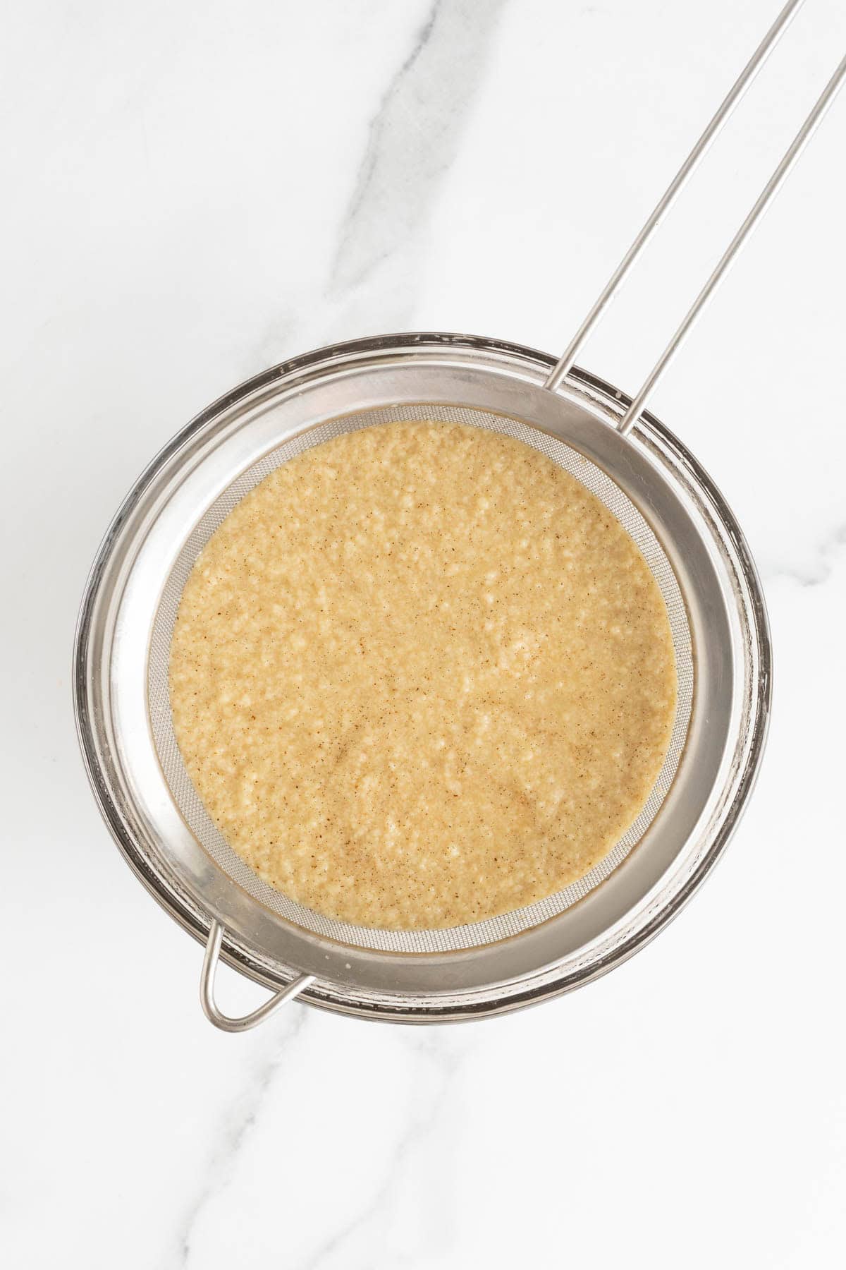 Custard being strained through a fine mesh sieve into a metal bowl