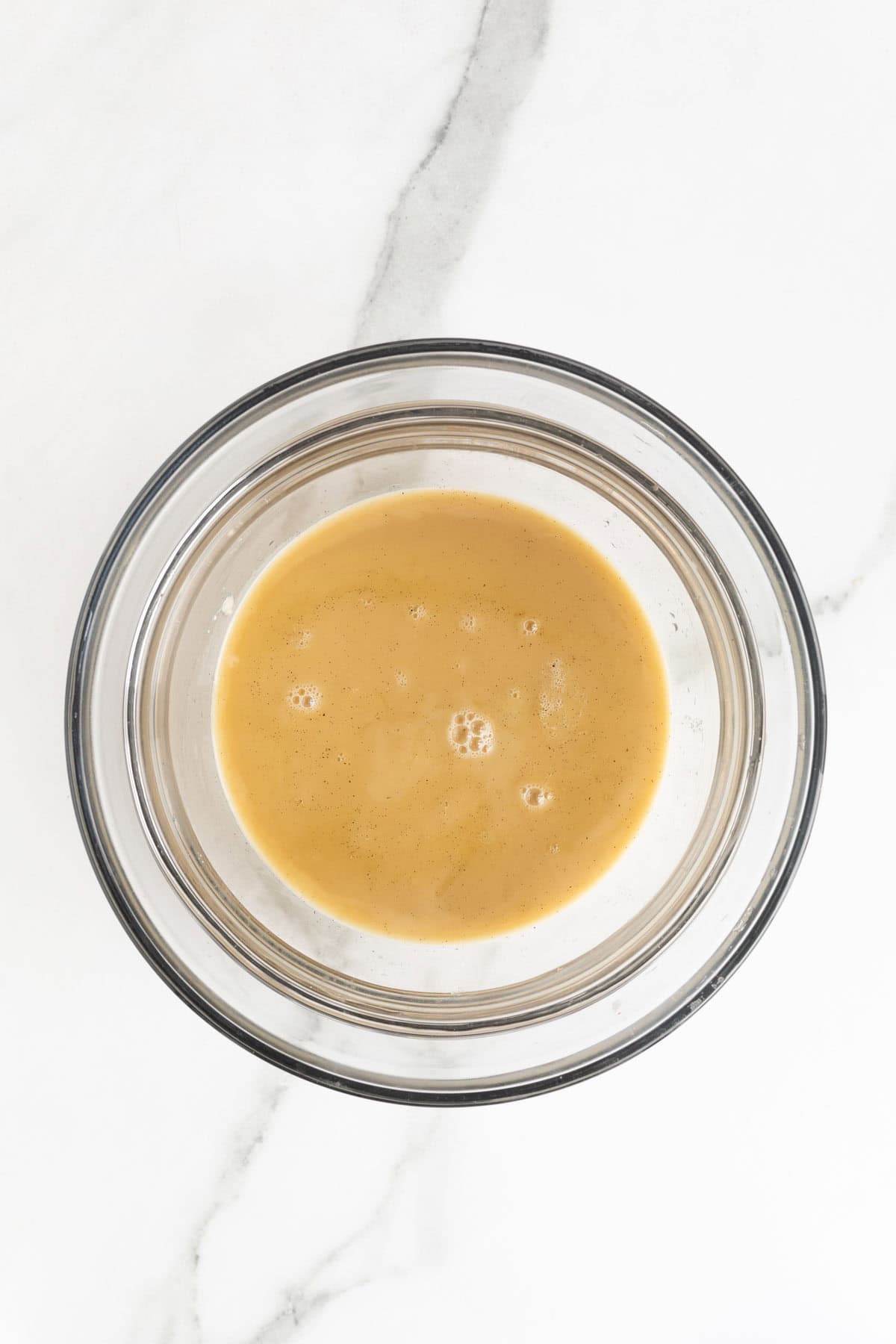 Vanilla custard mixture in a clear glass bowl after straining