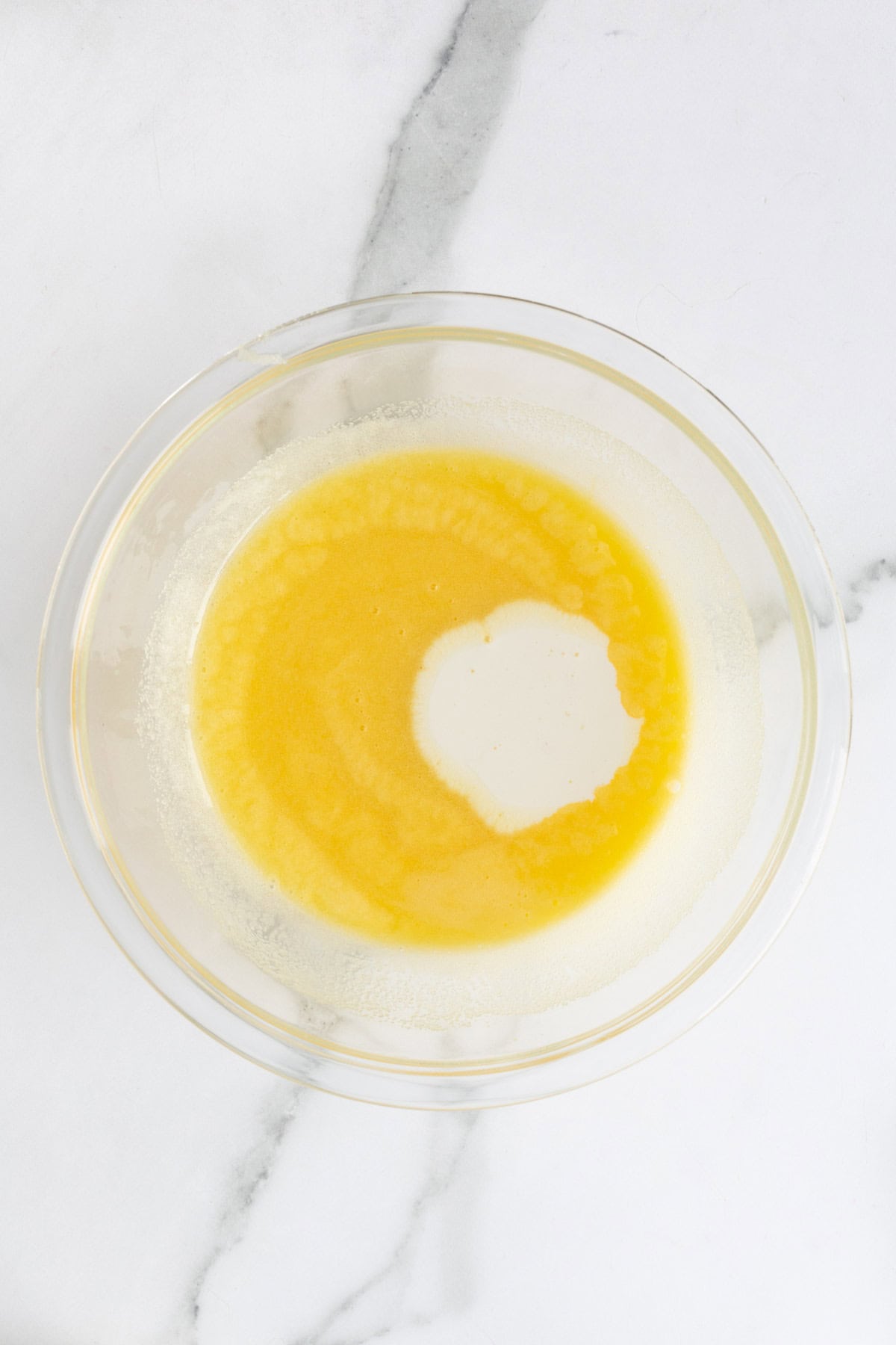 Heated cream mixture being added to the whisked egg mixture in a bowl