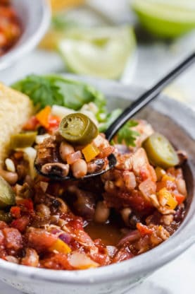 Close up of a bowl full of Chicken Chili with Black Eyed Peas and spoon full of it being pulled away
