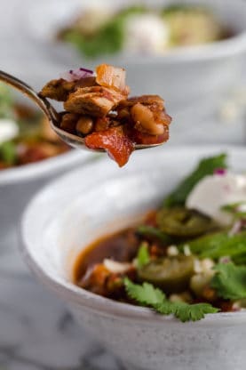 Close up of a spoon full of chicken chili with black eye peas being pulled away from a bowl of it