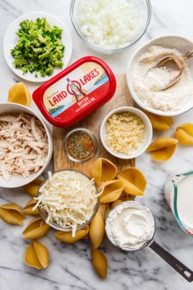 Overhead shot of the ingredients used to make this chicken stuffed shells recipe including pulled chicken pieces, cheese, broccoli and Land O Lakes butter all on top of a wooden cutting board