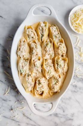 Overhead shot of uncooked chicken and stuffed shells dish contained in a white casserole dish