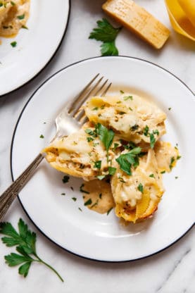 An individual serving of Flavorful chicken and broccoli are stuffed inside of tender pasta shells and smothered with cheese and a decadent cajun cream sauce on a white plate with a fork