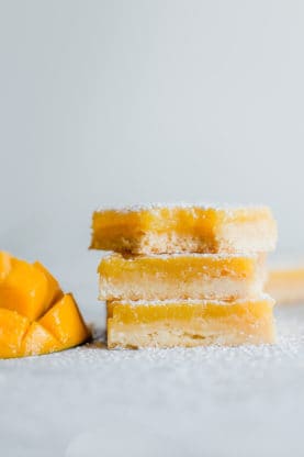 A stack of lemon bars on top of each other with sliced mango next to them