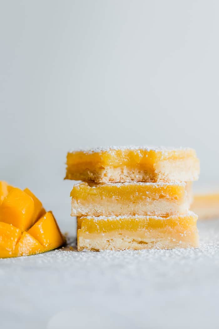 A stack of lemon bars on top of each other with sliced mango next to them