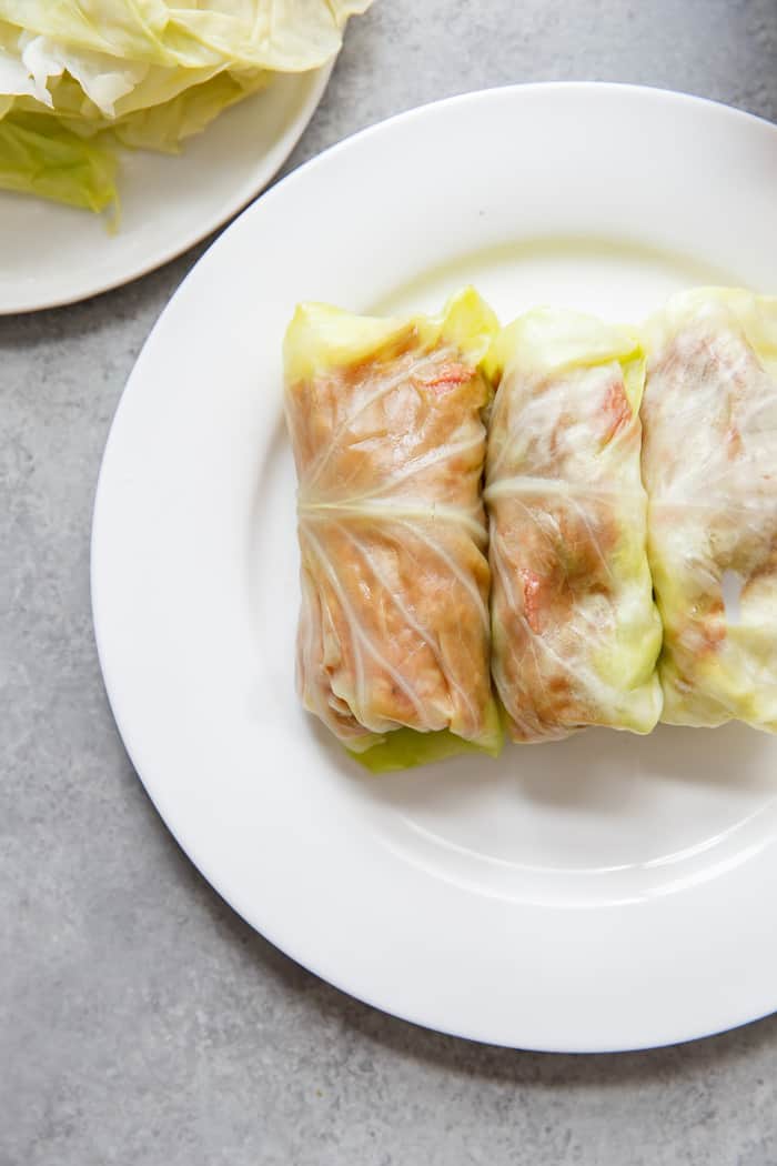 Three uncooked stuffed cabbage rolls sitting on a white plate. 