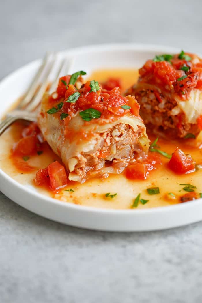 Stuffed Cabbage Rolls complimented with a tomato sauce are plated on white plate against gray background