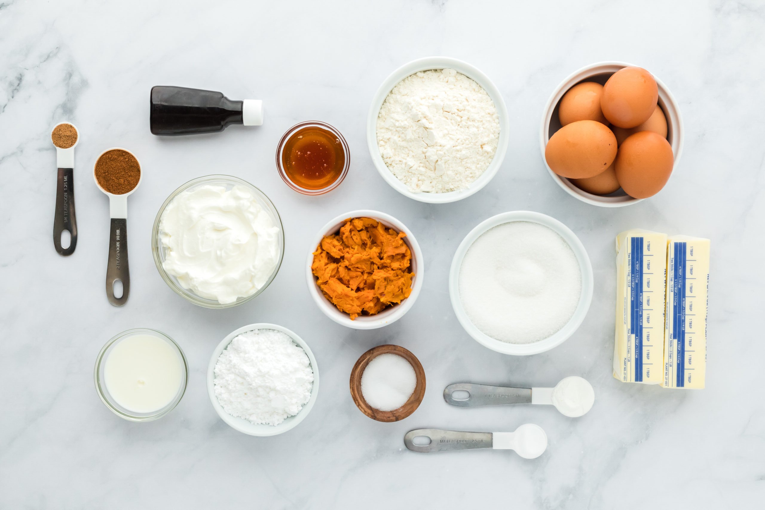 Sugar, eggs, butter, flour, vanilla, salt in white bowls on white countertop