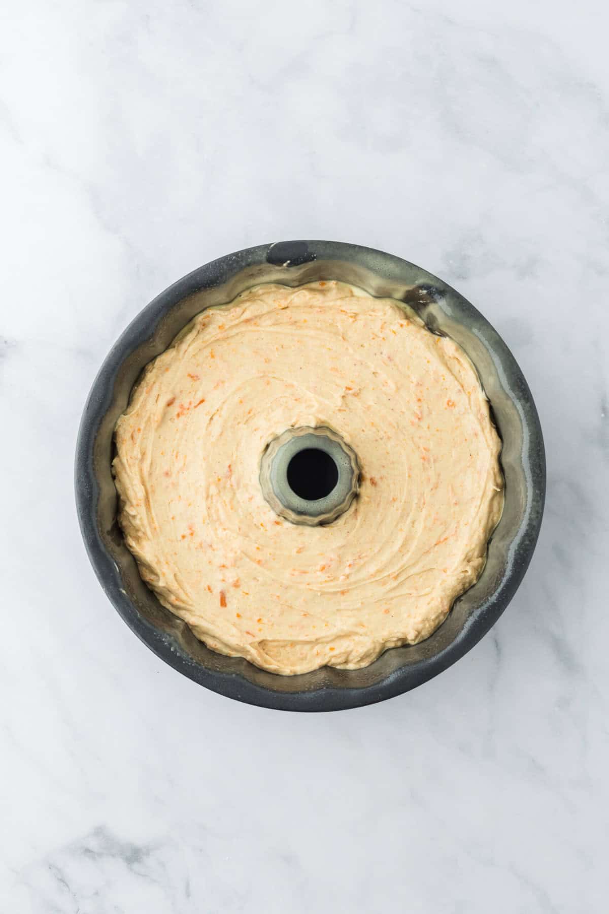 Pound cake batter added to a greased bundt pan on white countertop