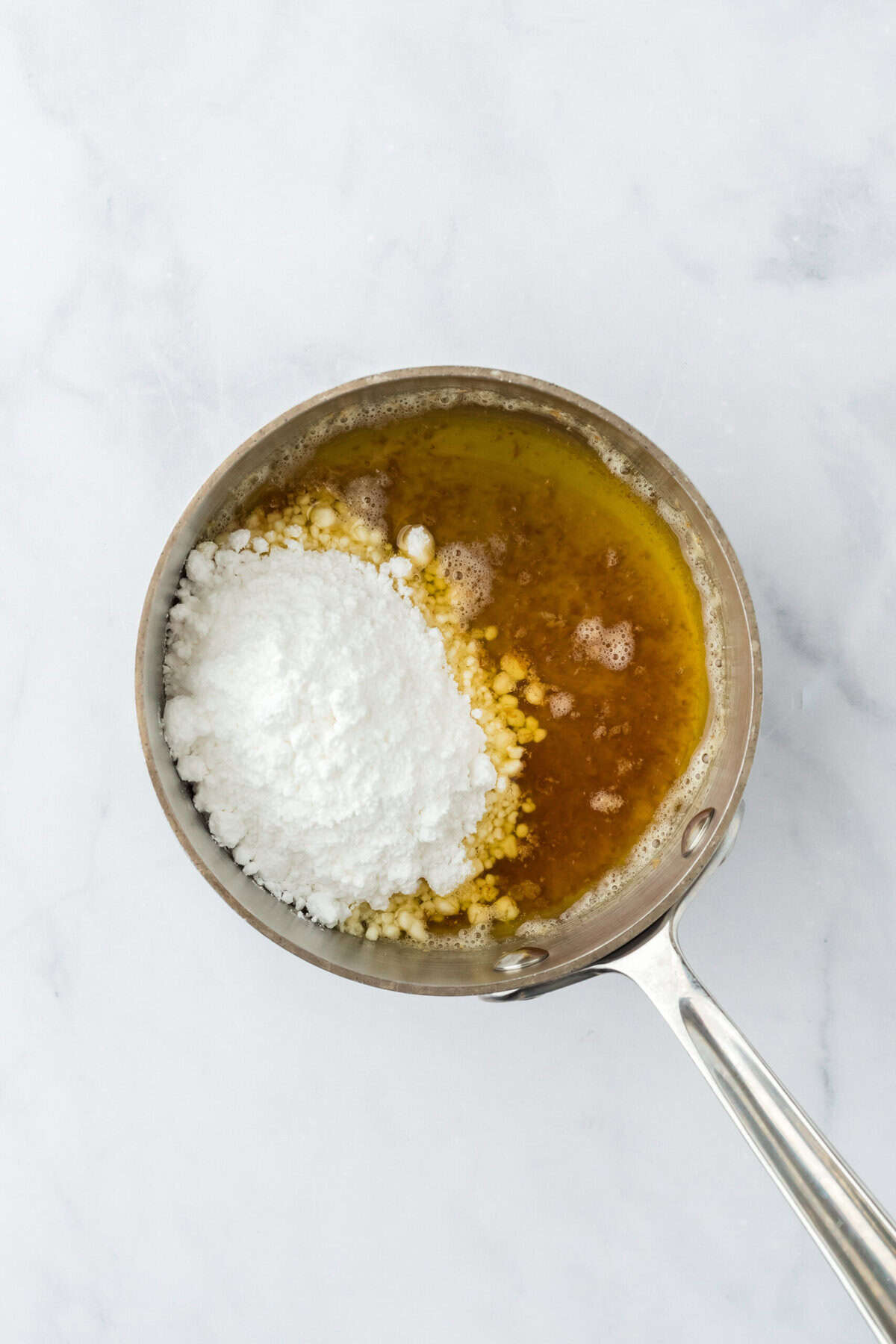 Powdered sugar added to brown butter in a saucepan on a white countertop