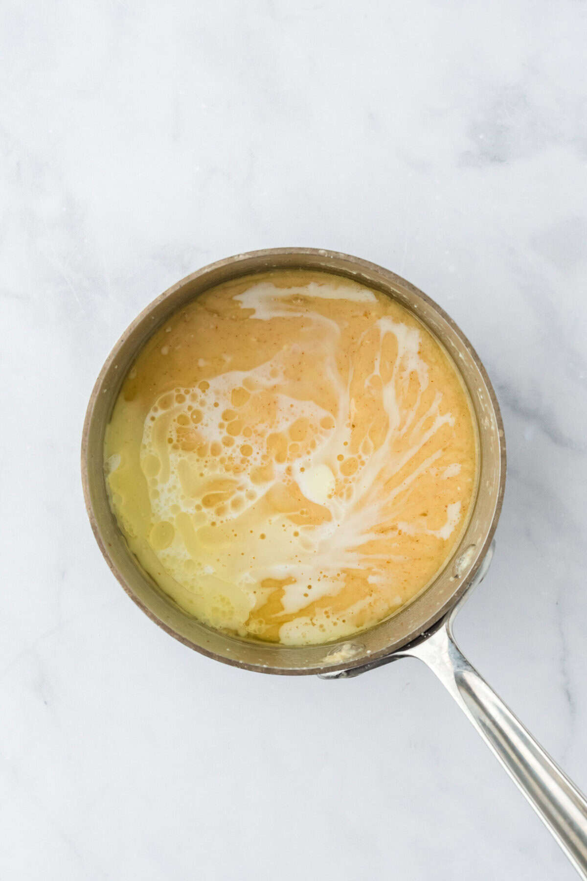 Milk added to brown butter glaze mixture in a saucepan on white countertop