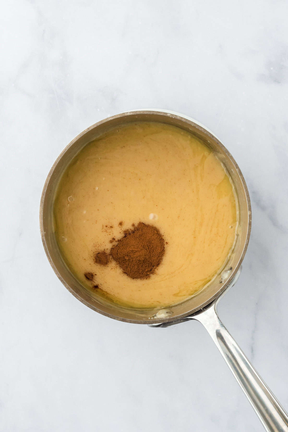 Cinnamon added to a brown butter glaze mixture in a saucepan on white countertop