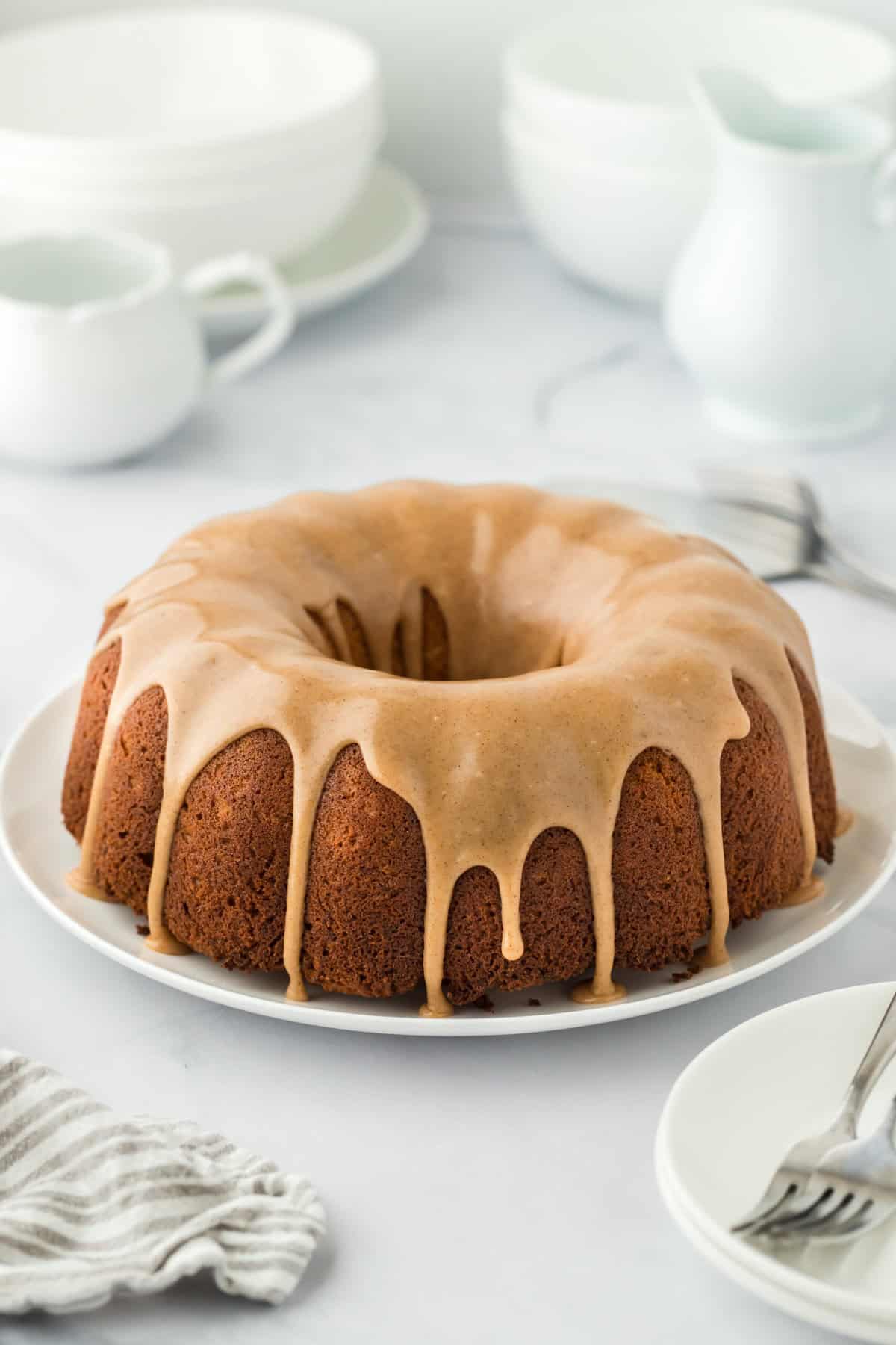 Whole sweet potato cake made in a bundt pan glazed on a white plate on white countertop with mugs in background