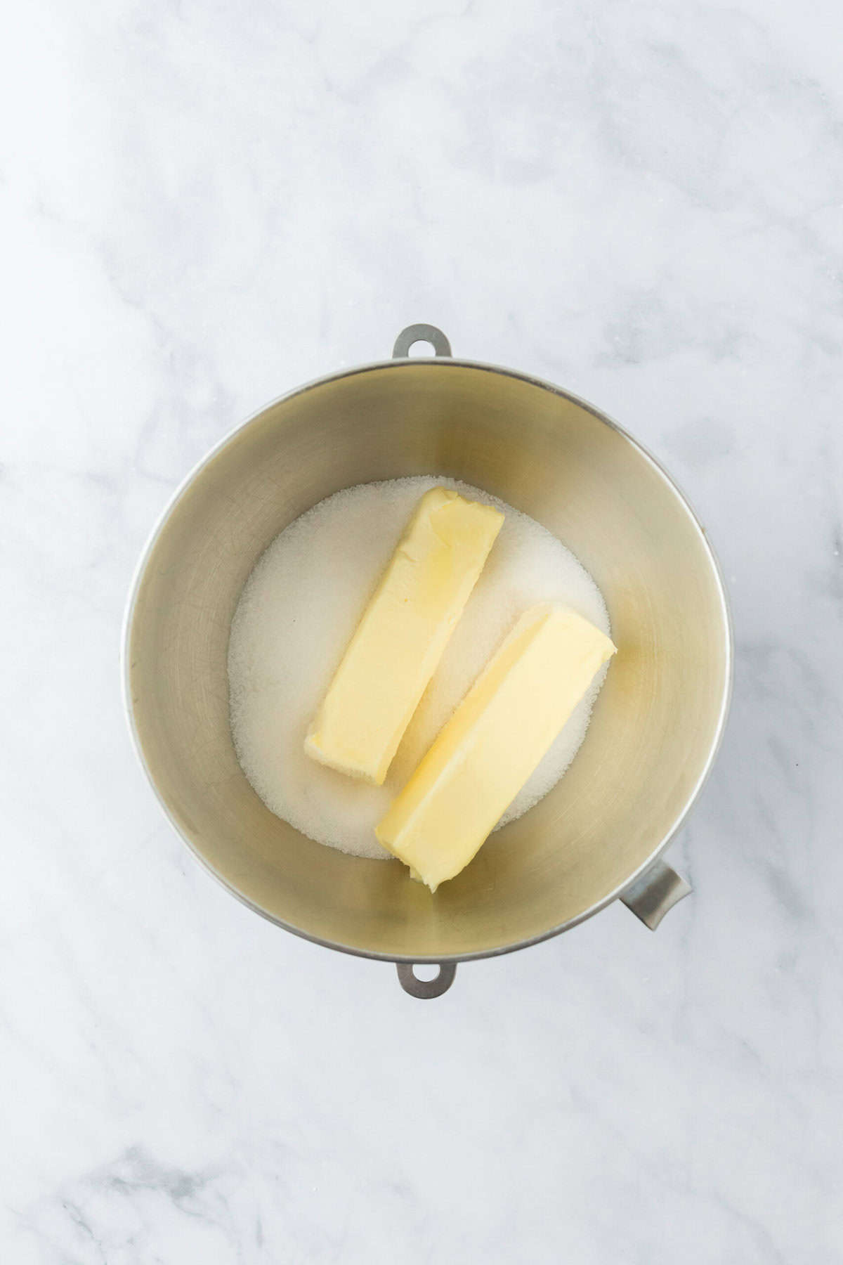 Butter and granulated sugar in a stand mixing bowl on white countertop