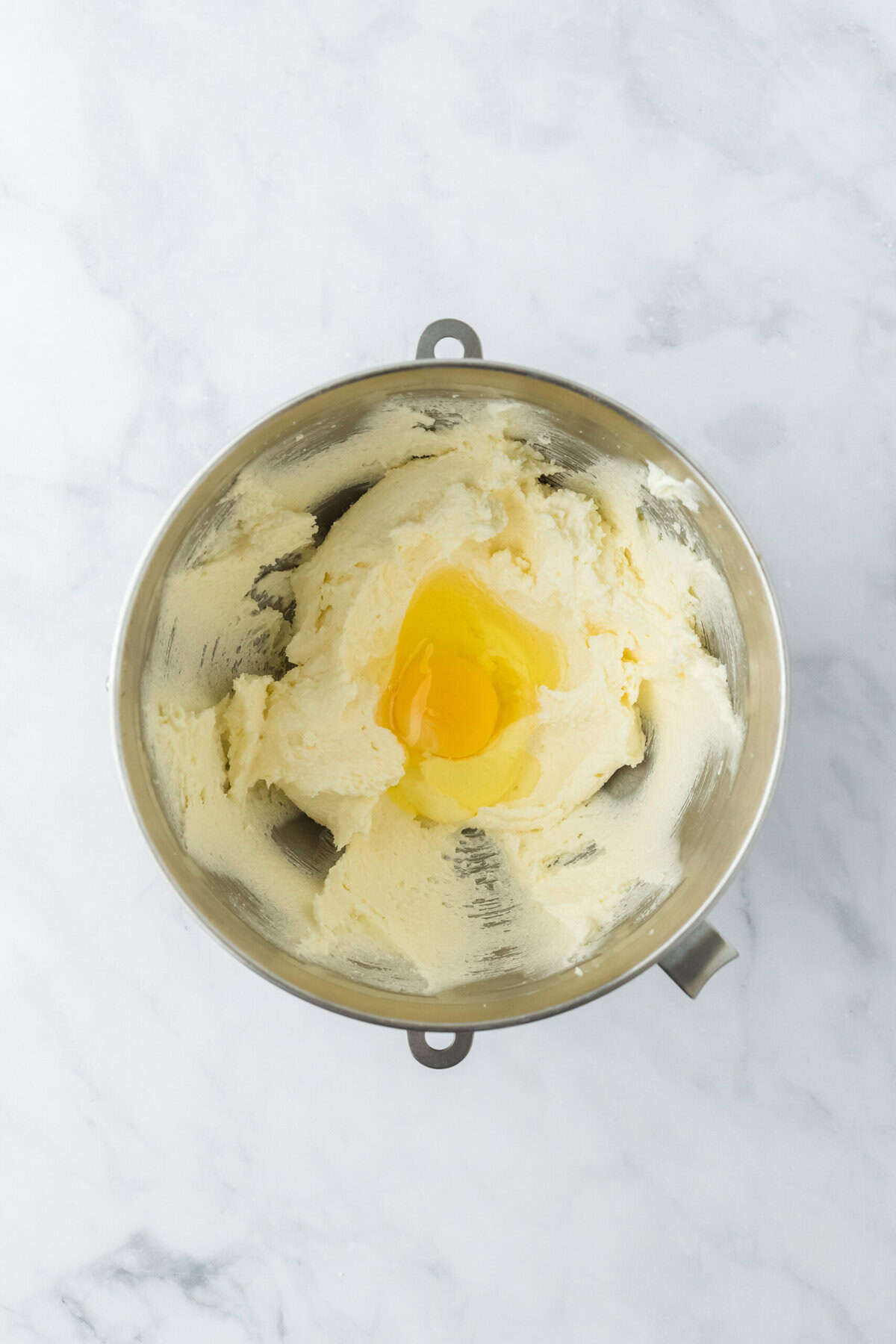 Egg in the creamed butter and sugar in stand mixing bowl on white countertop