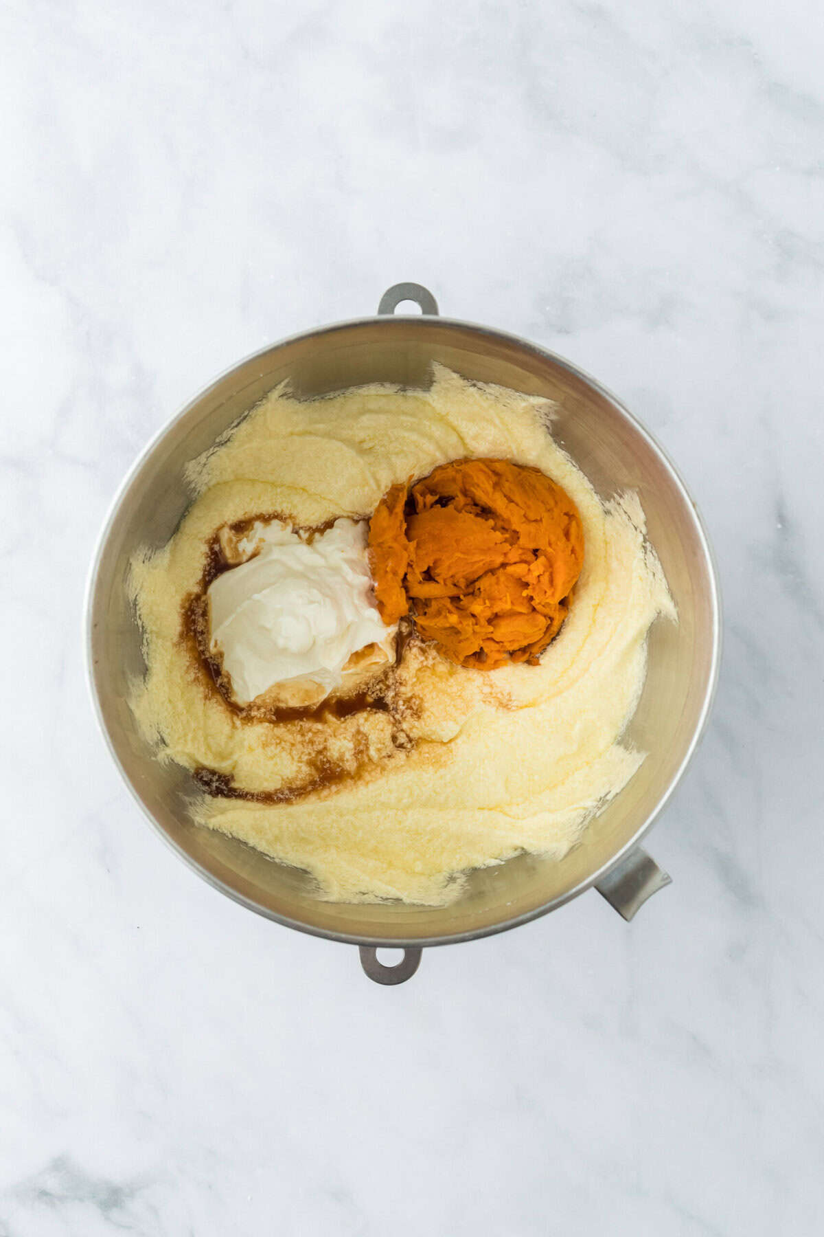 Mashed sweet potato and sour cream in a cake batter in a stand mixer on white countertop