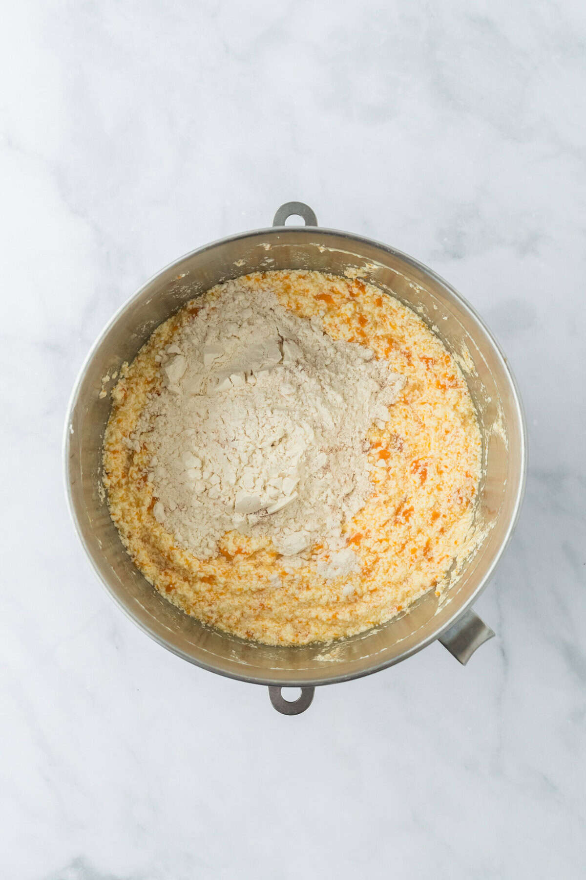 Dry ingredients added to sweet potato cake batter in stand mixing bowl on white countertop