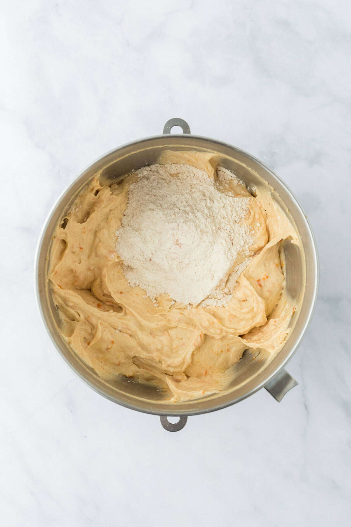 Remaining dry ingredients being added to sweet potato cake batter in stand mixing bowl on white countertop