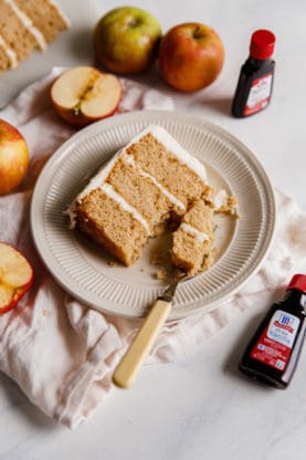 Baking extracts and a spiced apple cider flavored cake slice on a beige plate with sliced apples