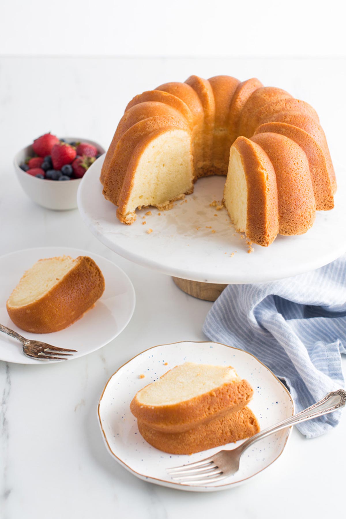 Sour cream pound cake on a white cake pedestal and plates served up around it.