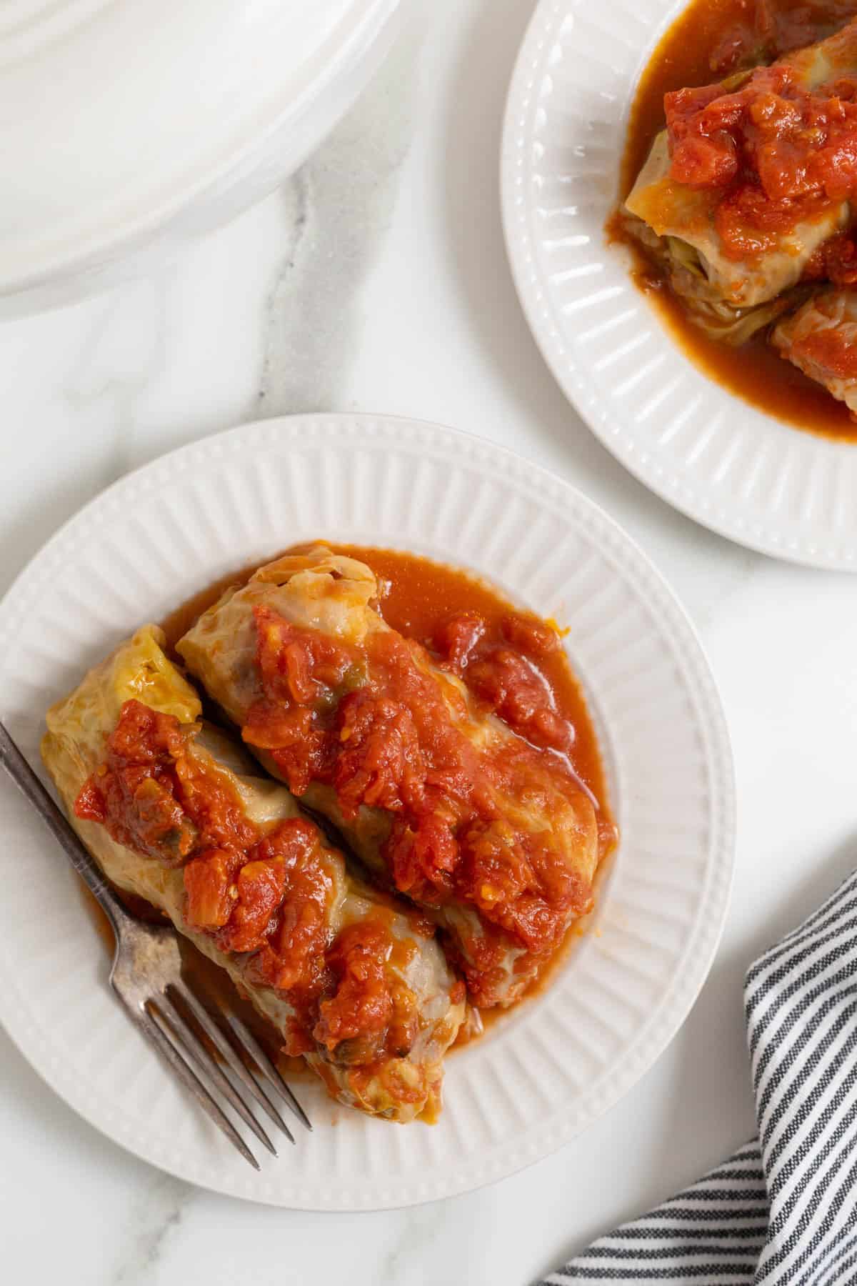 Overhead shot of stuffed cabbage rolls on white plates with a fork next to it