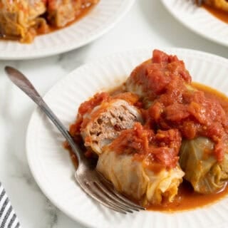 Stuffed cabbage rolls on white plates with a fork inside of it
