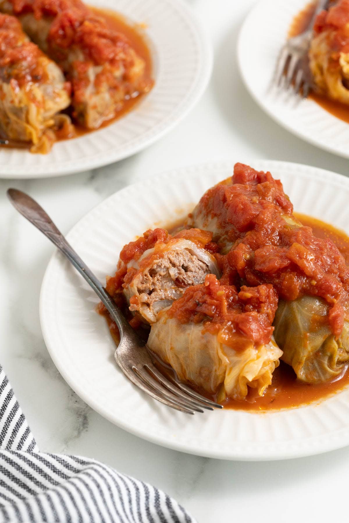 Stuffed cabbage rolls on white plates with a fork inside of it