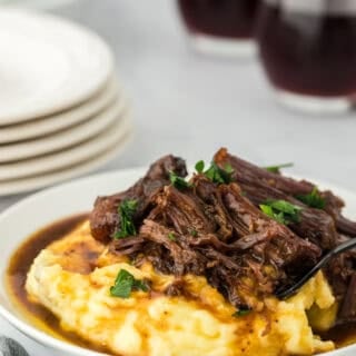 A large plate of a slow cooker Mississippi roast ready to serve over mashed potatoes