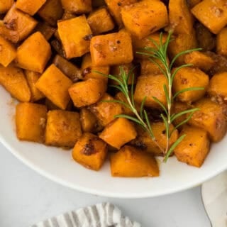 A close up of roasted butternut squash recipe on a white plate on white countertop