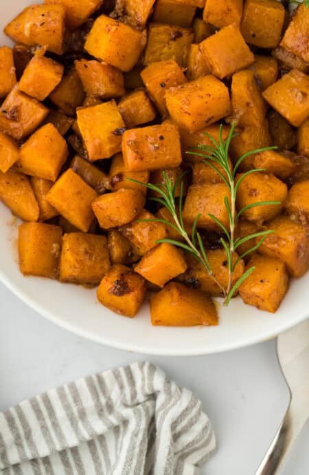 A close up of roasted butternut squash recipe on a white plate on white countertop