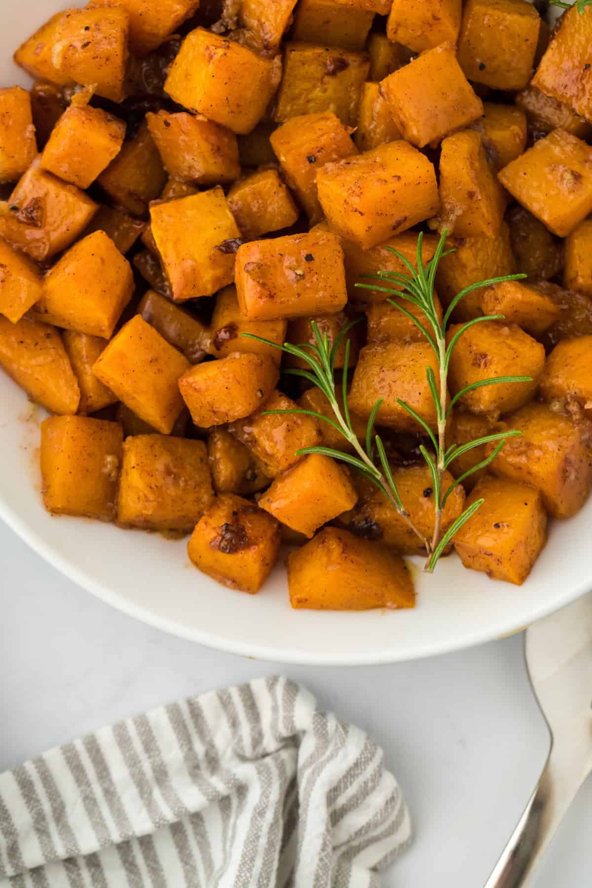 A close up of roasted butternut squash recipe on a white plate on white countertop