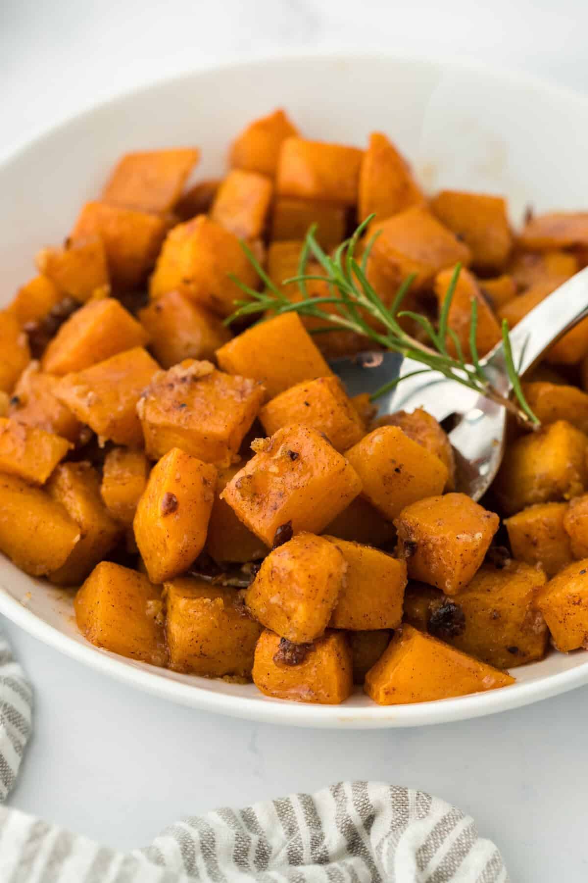 Roasted butternut squash in a white bowl with thyme ready to serve on white background