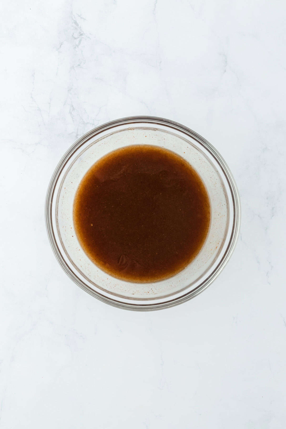 Whisked syrup mixture in glass bowl on white countertop