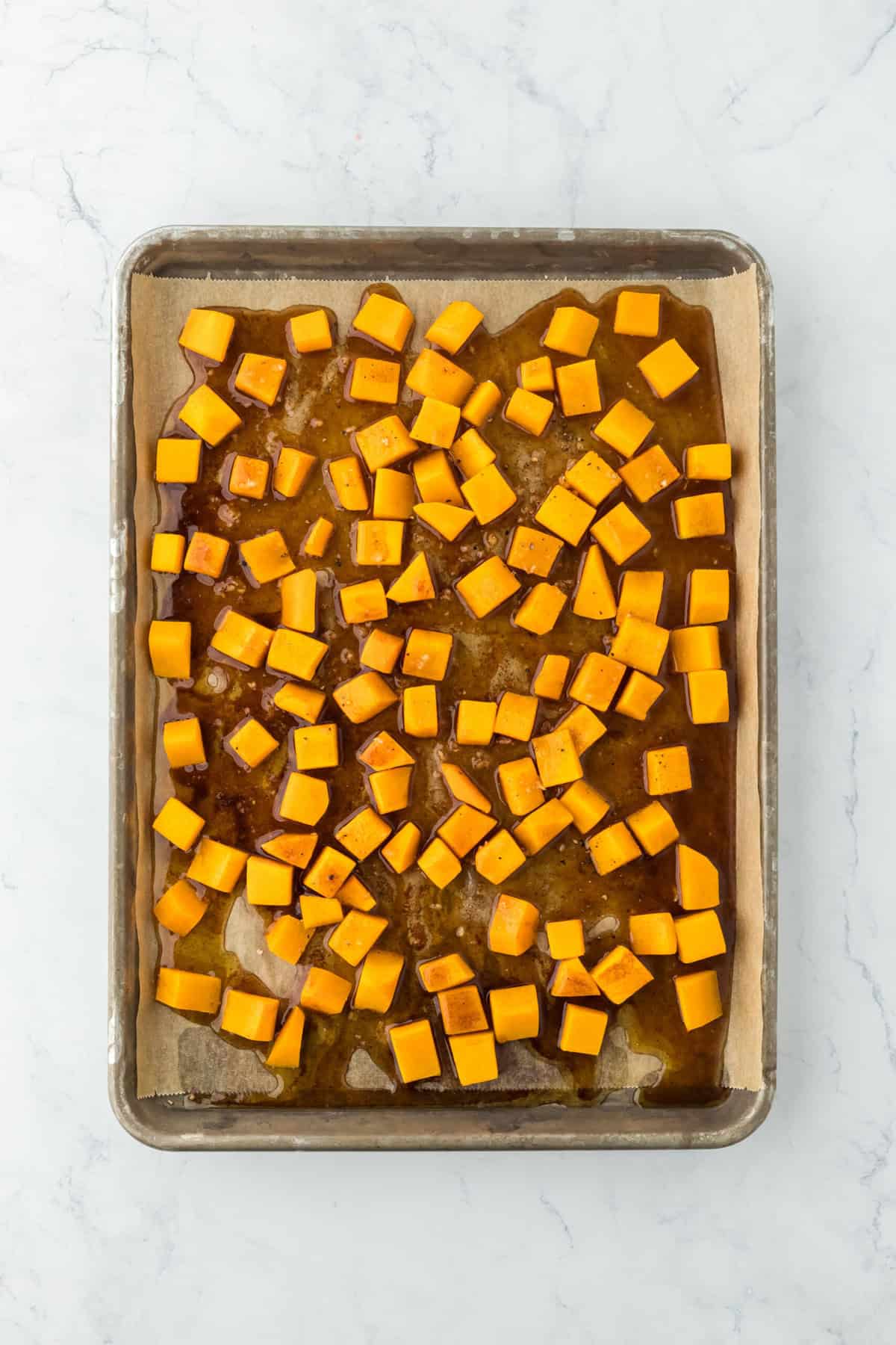 Butternut squash cubes on a baking dish with syrup drizzled over the top before roasting.