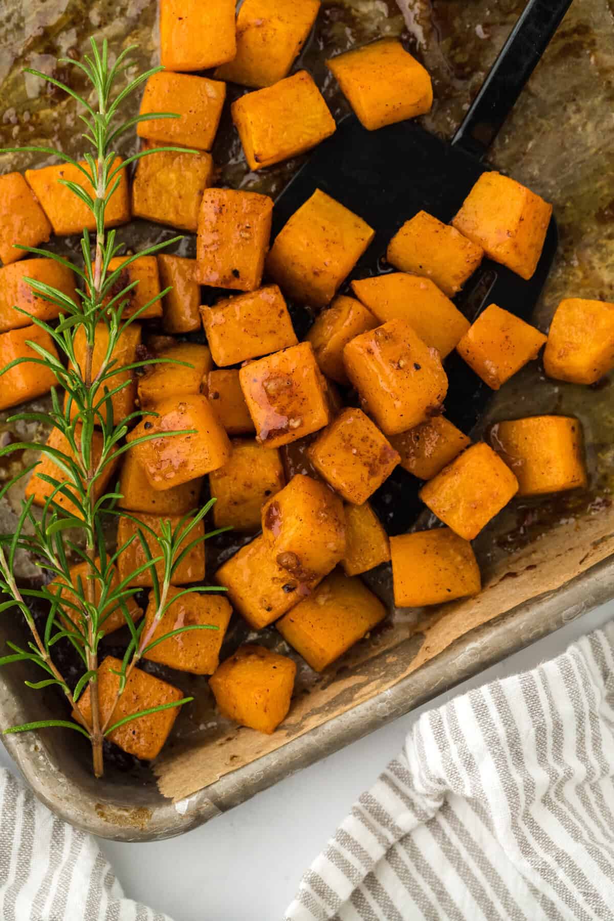 Baked butternut squash on a baking sheet with rosemary garnish