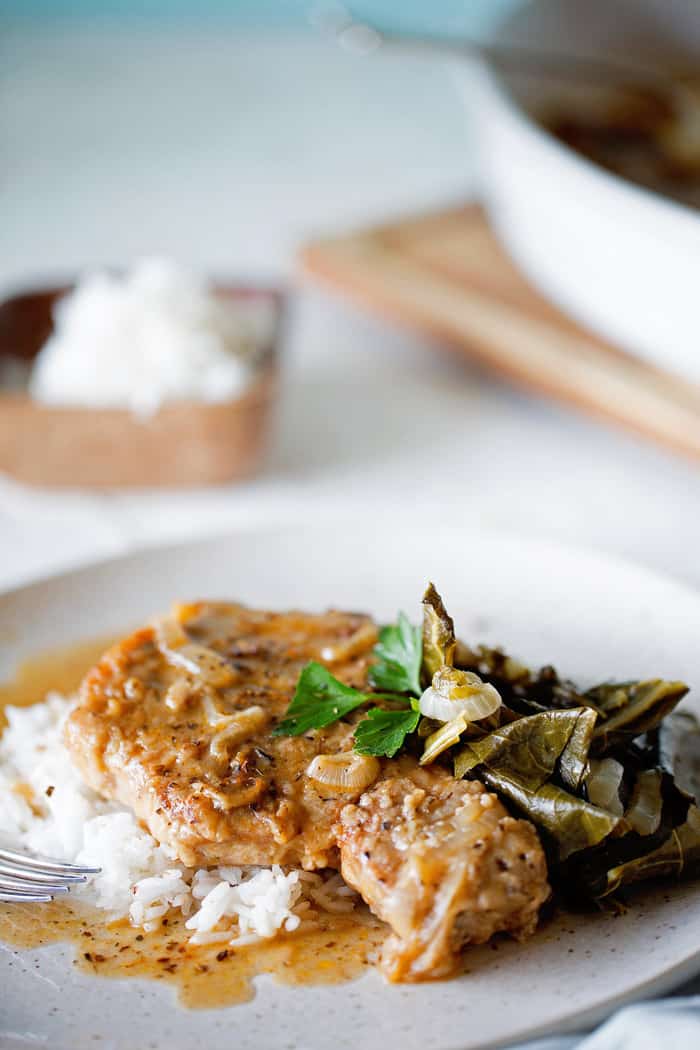 Close up of Southern Smothered Pork Chops Recipe over white rice with pork chop gravy and greens